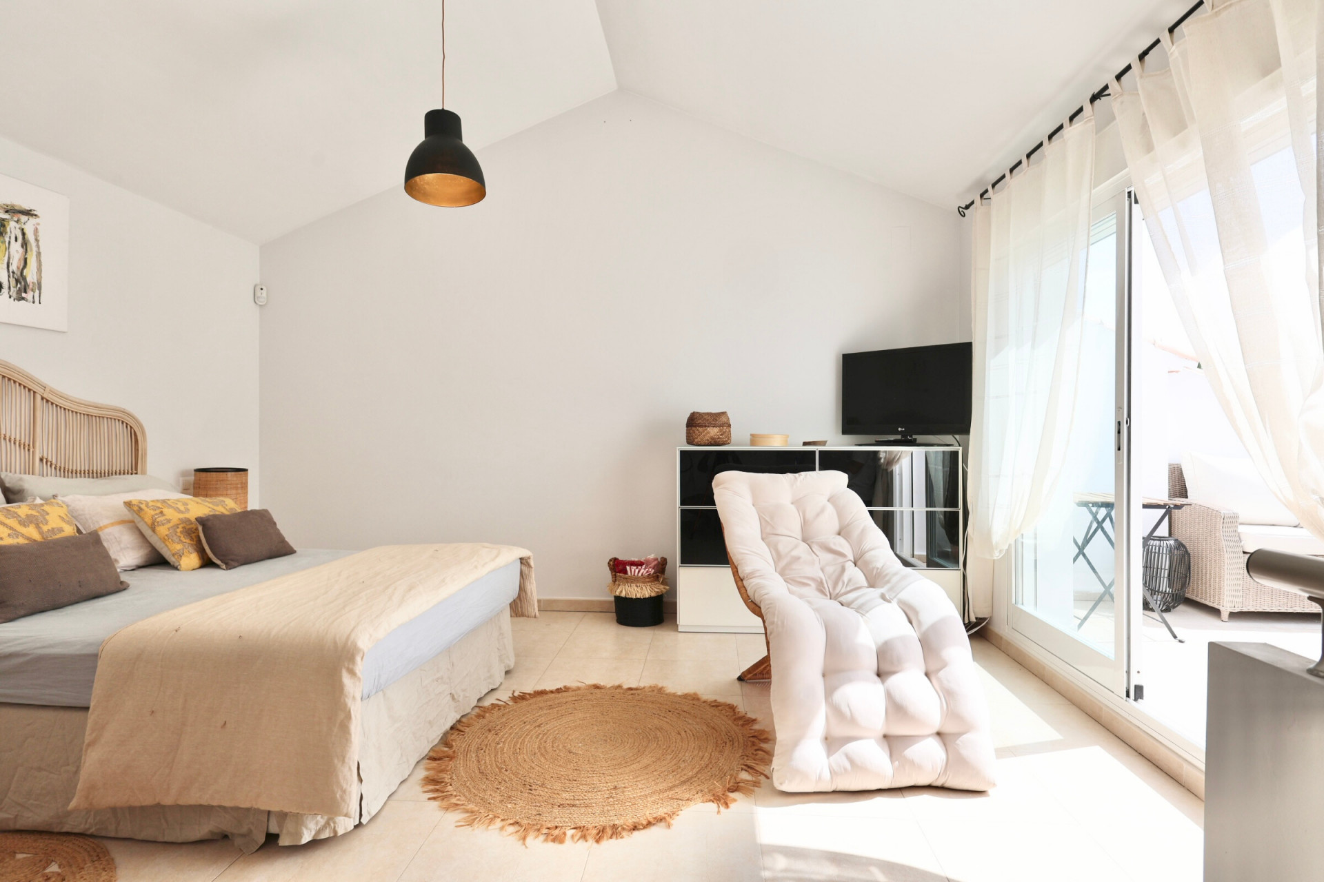Helles Schlafzimmer mit Rattanbett, Juteteppich und Zugang zur Terrasse.