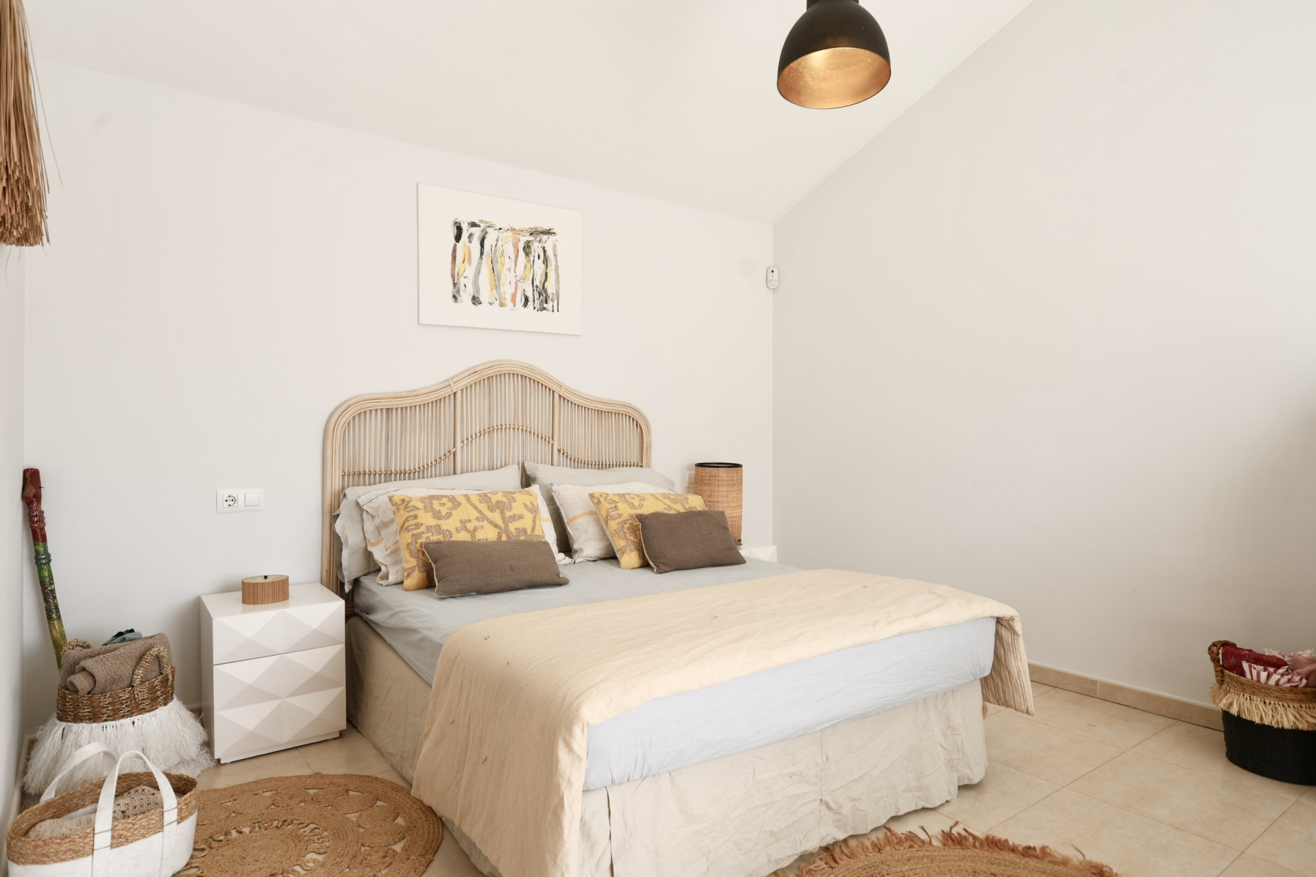 Helles Schlafzimmer mit Rattanbett, rundem Jute-Teppich und minimalistischer Dekoration.