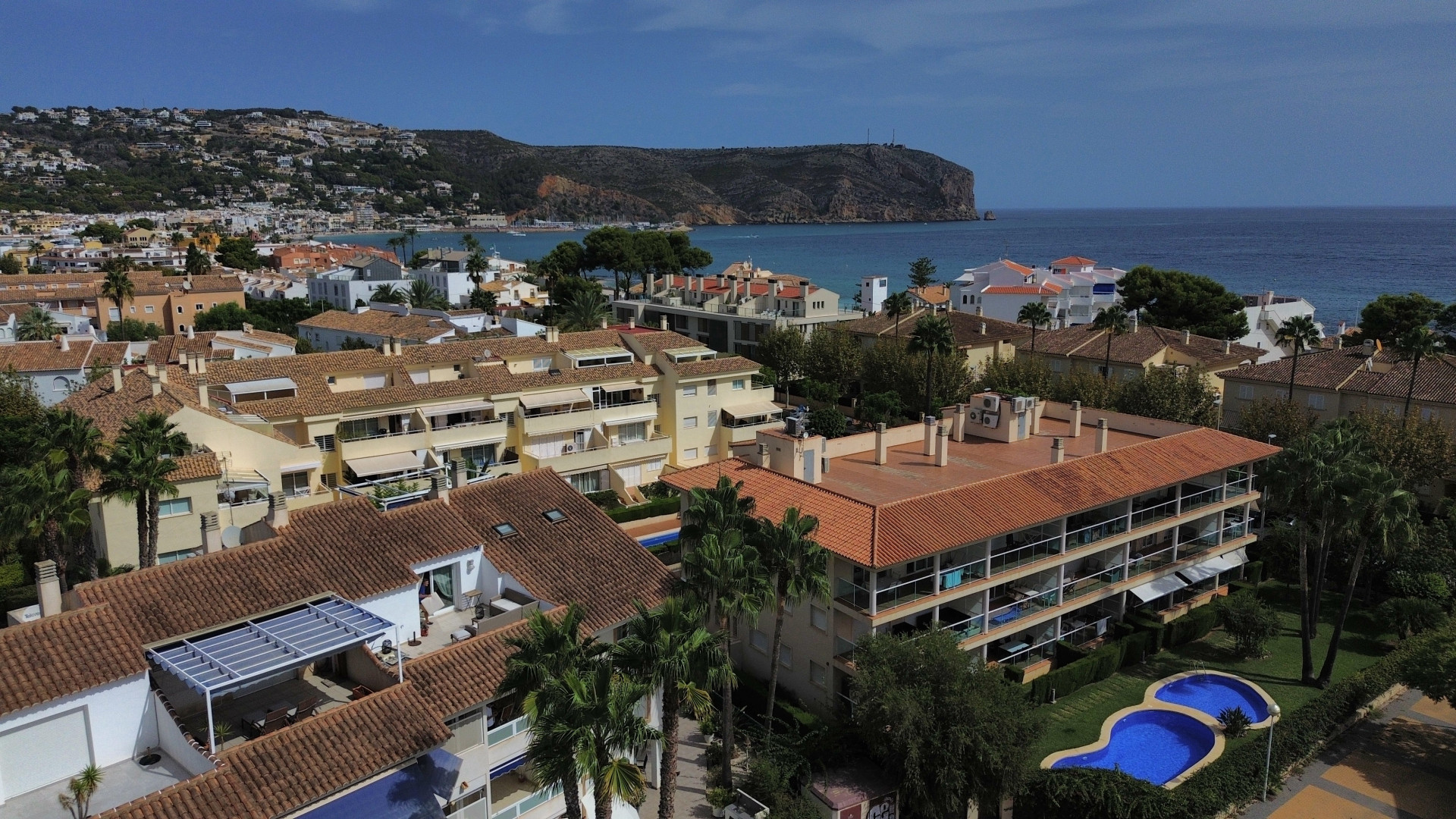 Luftaufnahme der Urbanisation mit Pool und Wohngebäuden mit roten Ziegeln in der Nähe der Küste von Jávea.