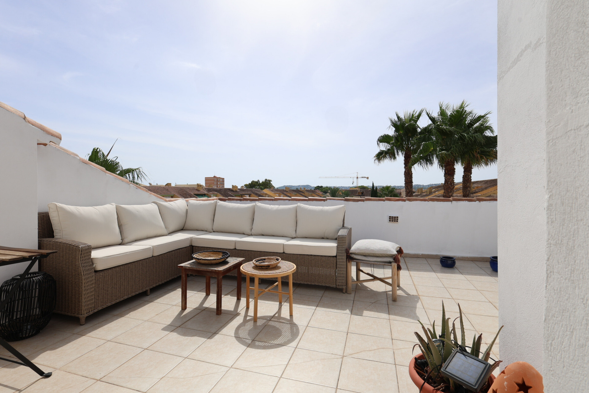 Sonnige, geflieste Terrasse mit Korbsitzgruppe und Blick auf Palmen.