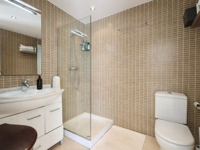 Badezimmer mit sandfarbenen Fliesenwänden, einer gläsernen Duschkabine und einem Waschtisch mit Marmorplatte.