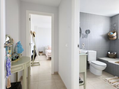 Flurdetail mit dekorativer Konsole und Blick ins Badezimmer mit grauen Fliesen und Schlafzimmer im Hintergrund.