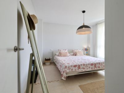 Helles Schlafzimmer mit Doppelbett, Bettwäsche mit Meeresmotiven und einer Hängelampe aus Korbgeflecht.