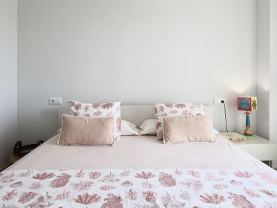 Helles Schlafzimmer mit Doppelbett, Bettwäsche mit Meeresmotiven und weißem Nachttisch mit dekorativer Lampe.