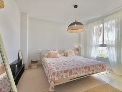 Helles Schlafzimmer mit Doppelbett, gemusterter Bettwäsche und einer Hängelampe aus Korbgeflecht.