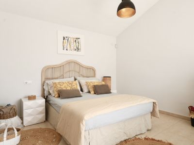 Helles Schlafzimmer mit Rattanbett, rundem Jute-Teppich und minimalistischer Dekoration.