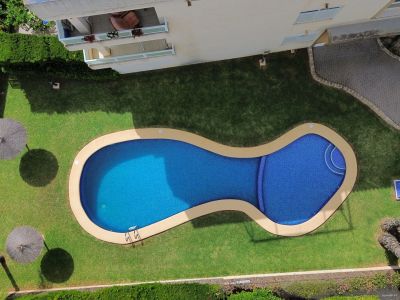 Luftaufnahme des organisch geformten Pools mit gepflegtem Rasen, Strohschirmen und üppigem Grün.