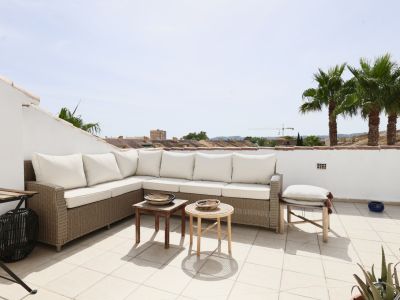 Terrasse mit Korbsitzgruppe und weißen Kissen, mit Blick auf Palmen und Dächer.