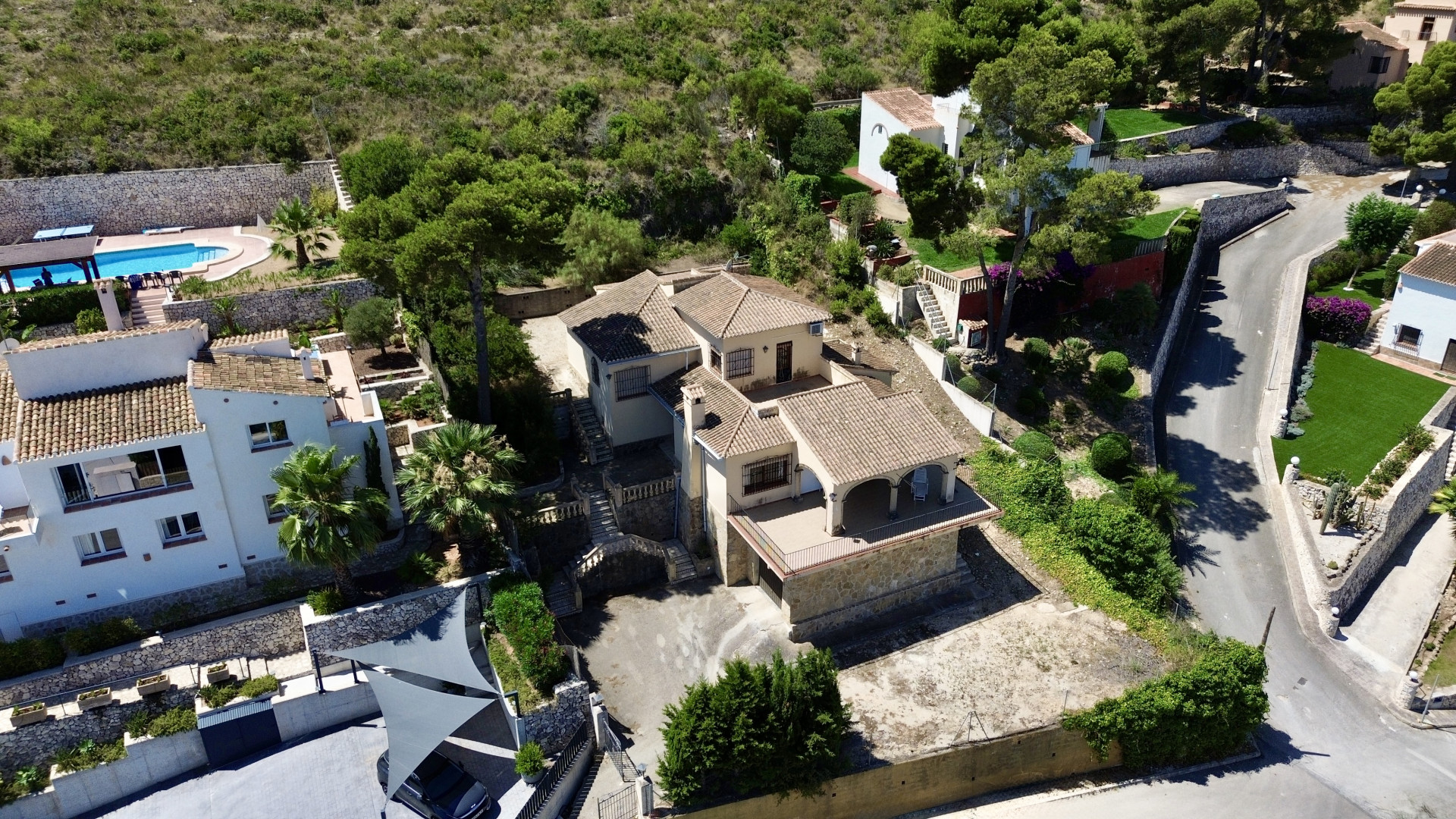 Luftaufnahme der mehrstöckigen Villa mit traditionellen Ziegeldächern, mehreren Terrassen und Hangbereichen, eingebettet in mediterrane Vegetation.