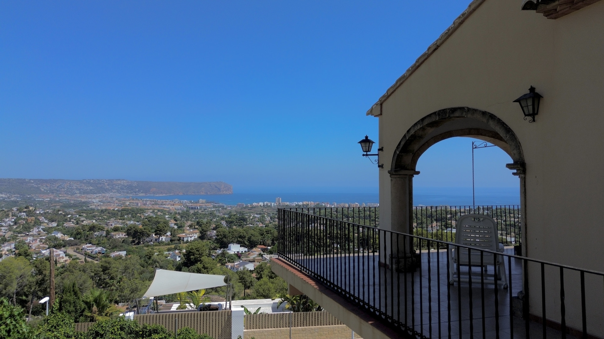 Überdachte Terrasse mit Panoramablick auf Meer, Stadt und Landschaft, eingerahmt von einem Steinbogen und schmiedeeisernem Geländer.