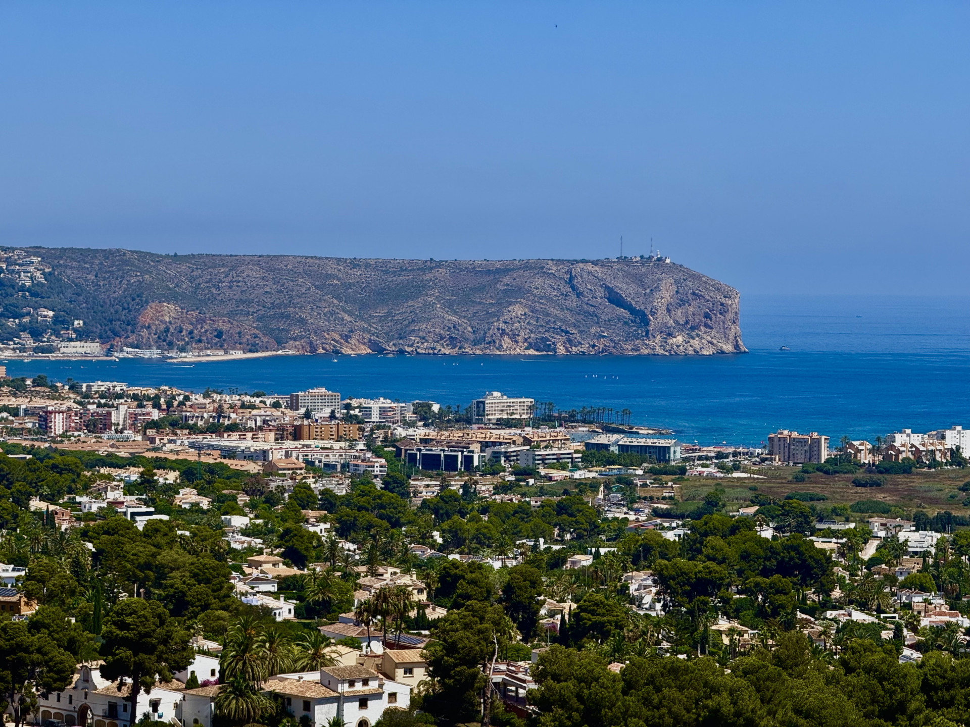 Weitläufiger Panoramablick auf die Wohnlandschaft von Jávea, das tiefblaue Mittelmeer mit Booten und das markante Felskap mit seinem Leuchtturm.