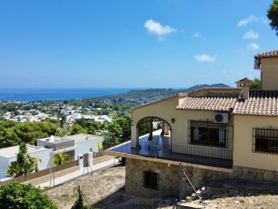 Außenansicht der Villa mit überdachter Terrasse, Bogenarchitektur und schwarzen Geländern. Das Hanggrundstück bietet Panoramablicke auf das Meer, die Stadt und die Berge.