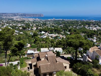 Luftaufnahme von Jávea, die traditionelle Villen mit Terrakottadächern zwischen Pinien zeigt, mit dem Mittelmeer und dem Cabo de San Antonio im Hintergrund.