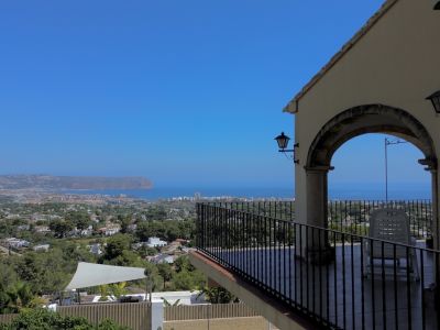 Überdachte Terrasse mit Panoramablick auf Meer, Stadt und Landschaft, eingerahmt von einem Steinbogen und schmiedeeisernem Geländer.