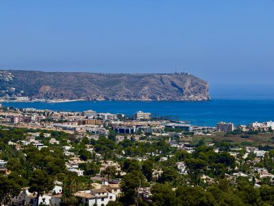 Weitläufiger Panoramablick auf die Wohnlandschaft von Jávea, das tiefblaue Mittelmeer mit Booten und das markante Felskap mit seinem Leuchtturm.
