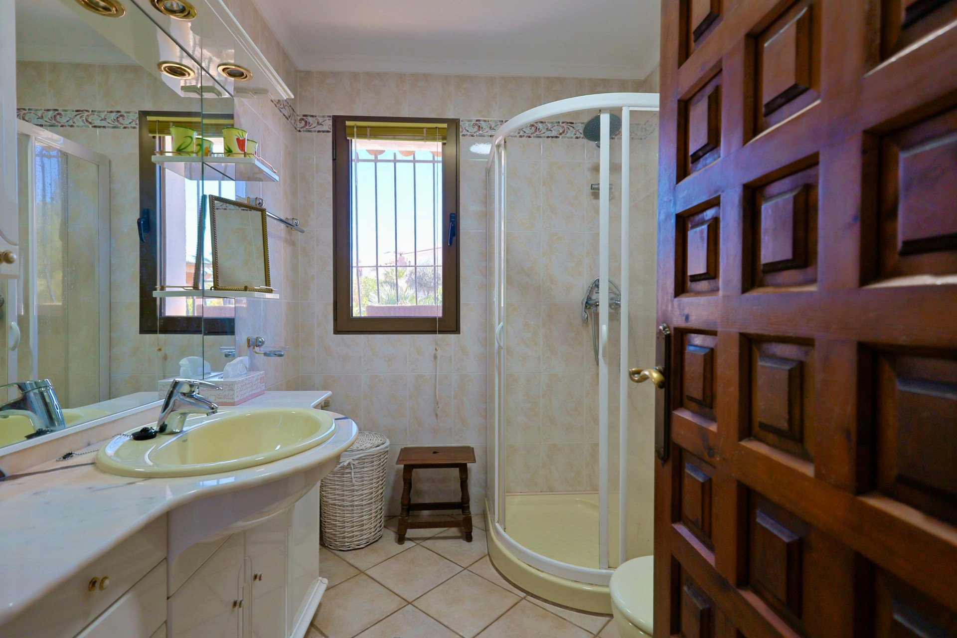 Badezimmerdetail mit gelbem Waschbecken, Eckdusche und geschnitzter Holztür.