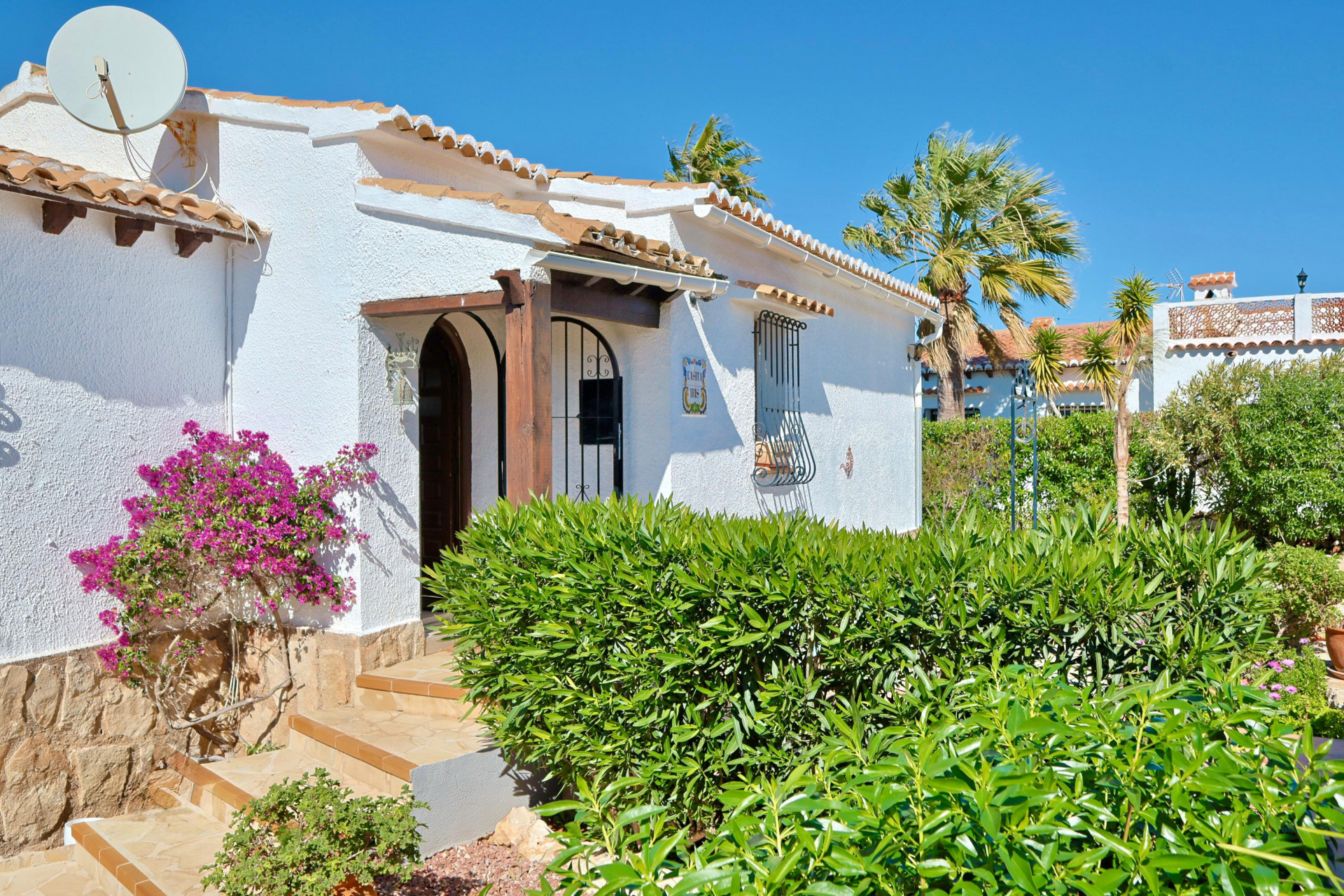 Fassade einer mediterranen Villa mit Bougainvillea und Holzbogeneingang.