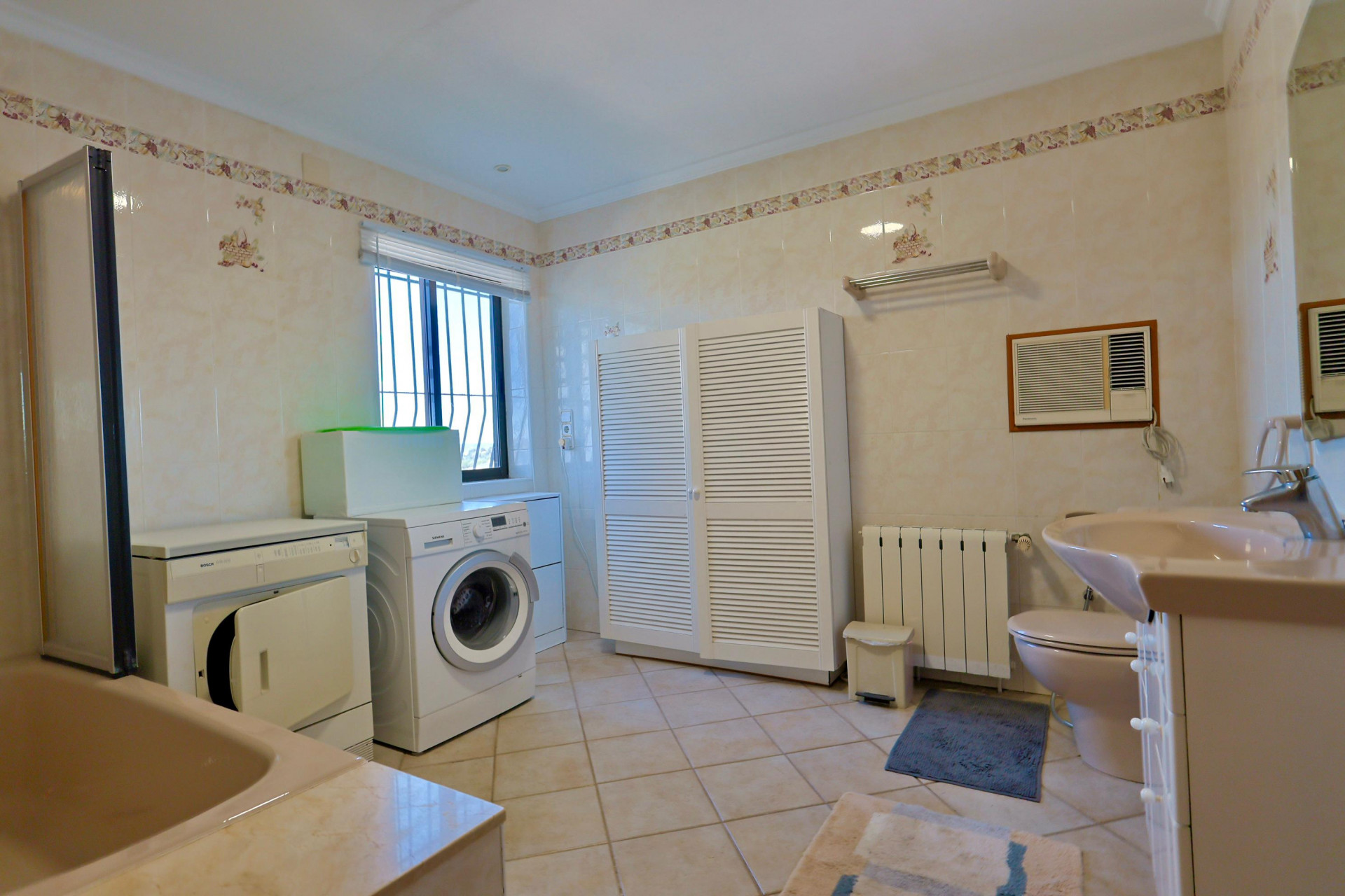 Funktionales Badezimmer mit Waschmaschine, Trockner und geräumigem, weißem Lamellenschrank.