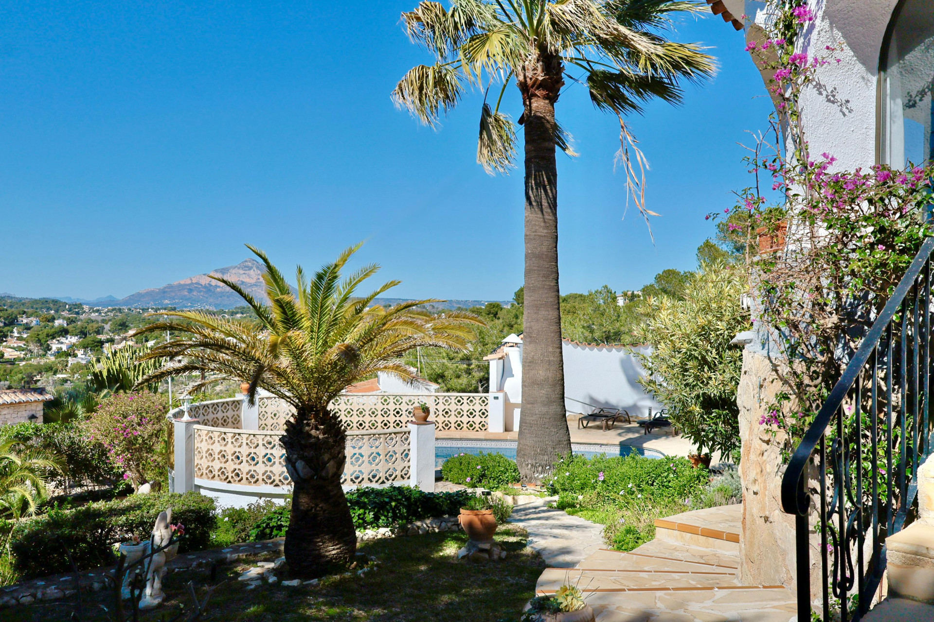 Gartenblick mit Pool und Palmen, der die mediterrane Vegetation und die Berglandschaft im Hintergrund hervorhebt.