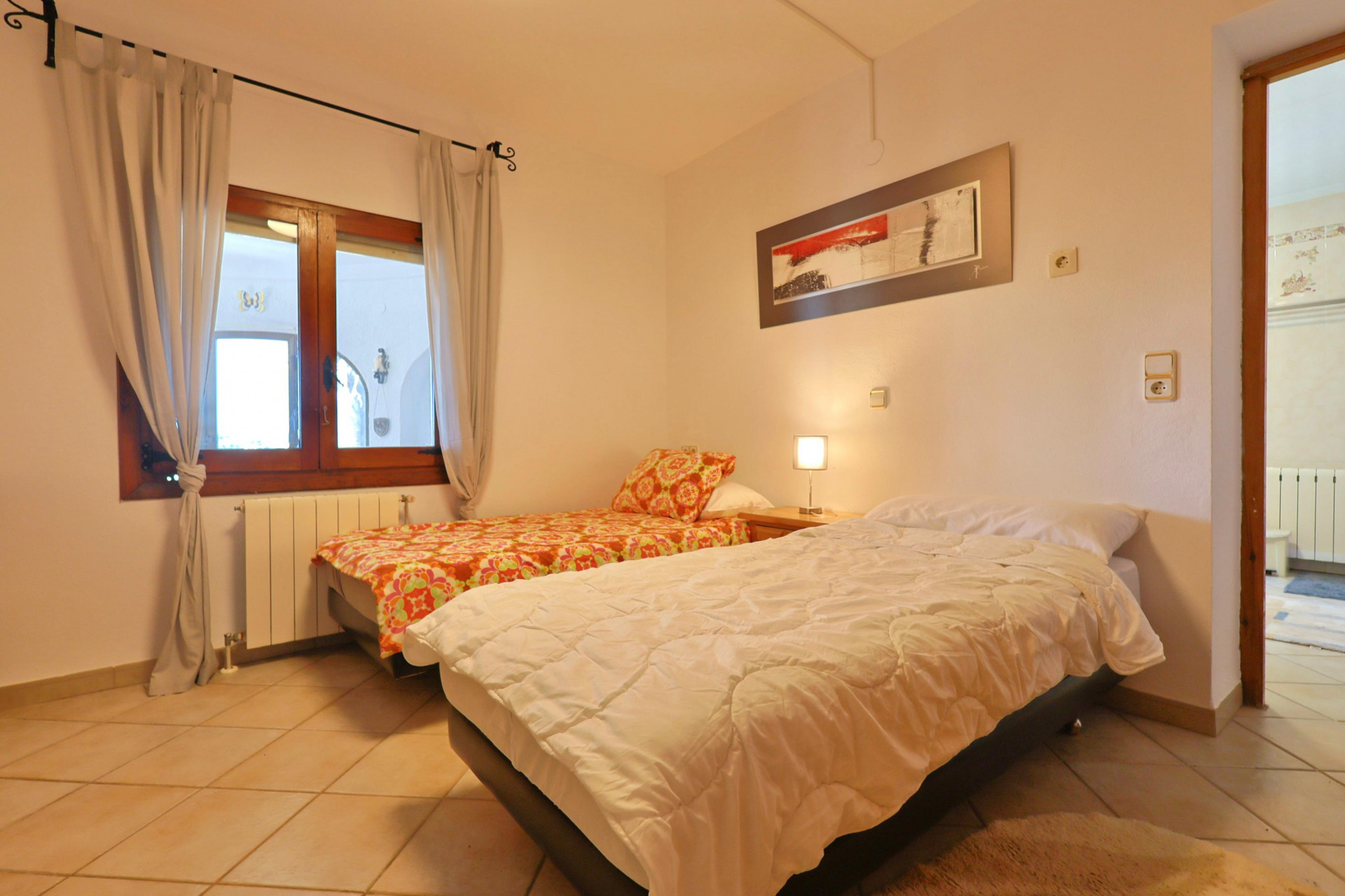Helles Schlafzimmer mit Einzelbetten, Holzfensterrahmen und Fliesenboden.