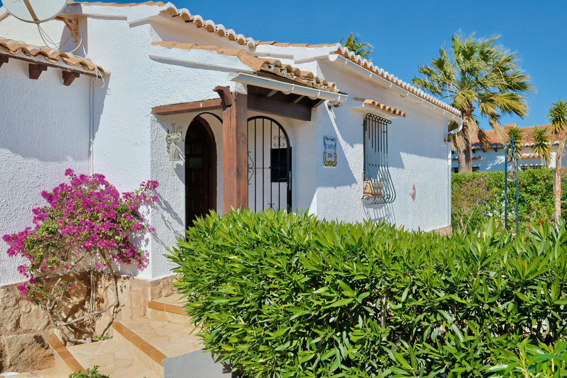 Mediterrane Villenfassade mit Bougainvillea und Holzdetails.