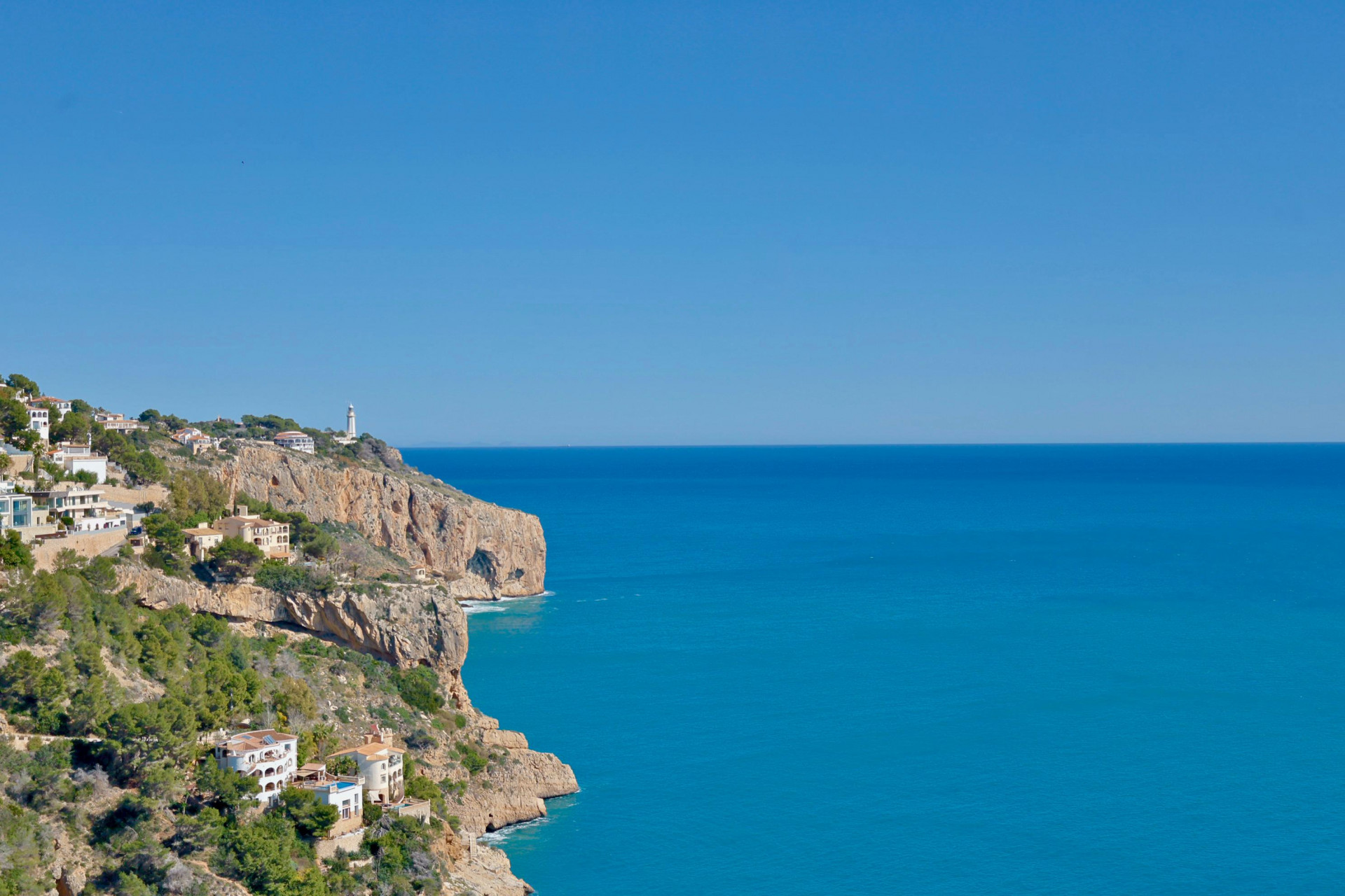 Panoramablick auf die felsige Küstenlinie und das Mittelmeer von Jávea aus, mit weißen Häusern am Hang.