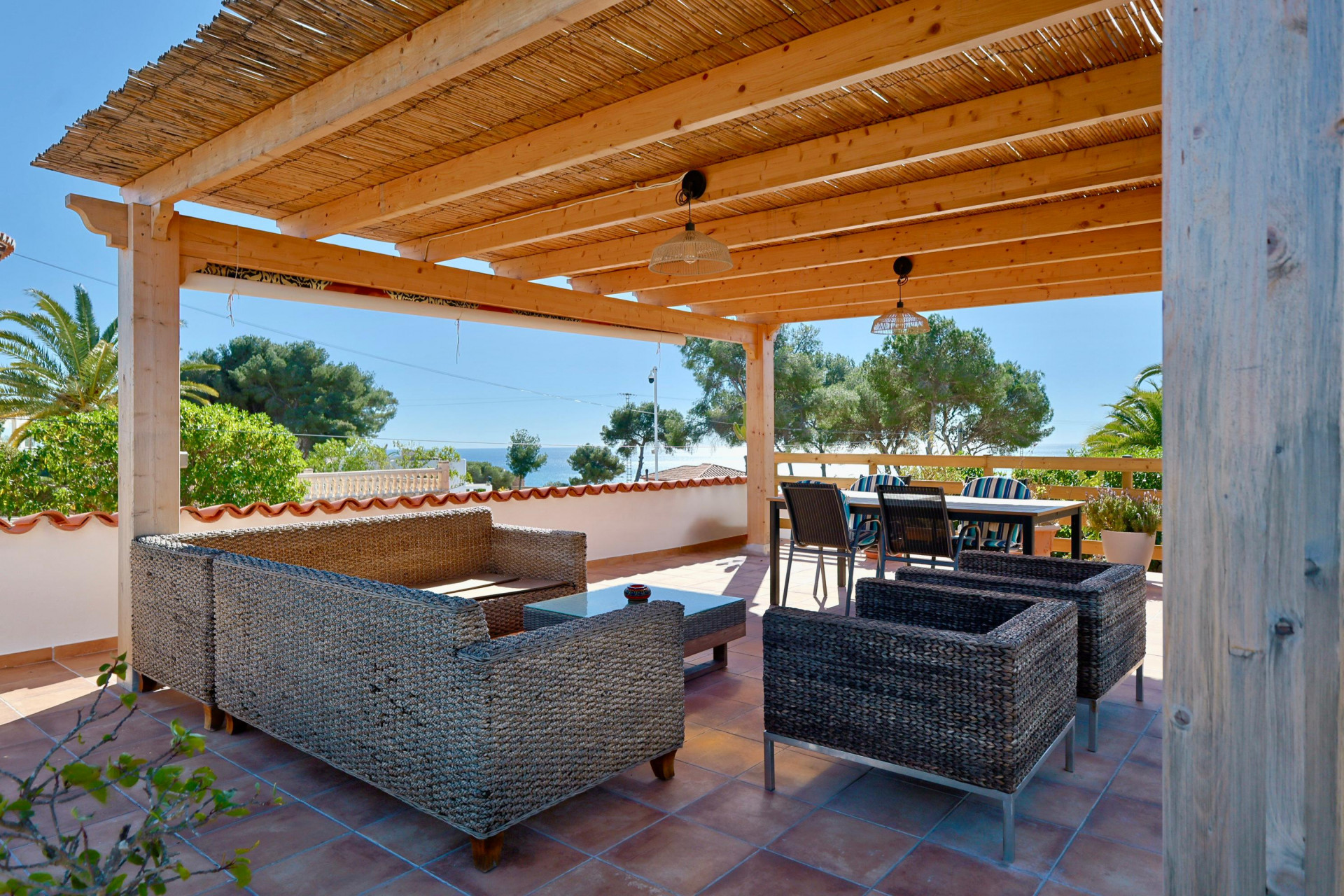 Überdachte Terrasse mit Rattanmöbeln und Meerblick.