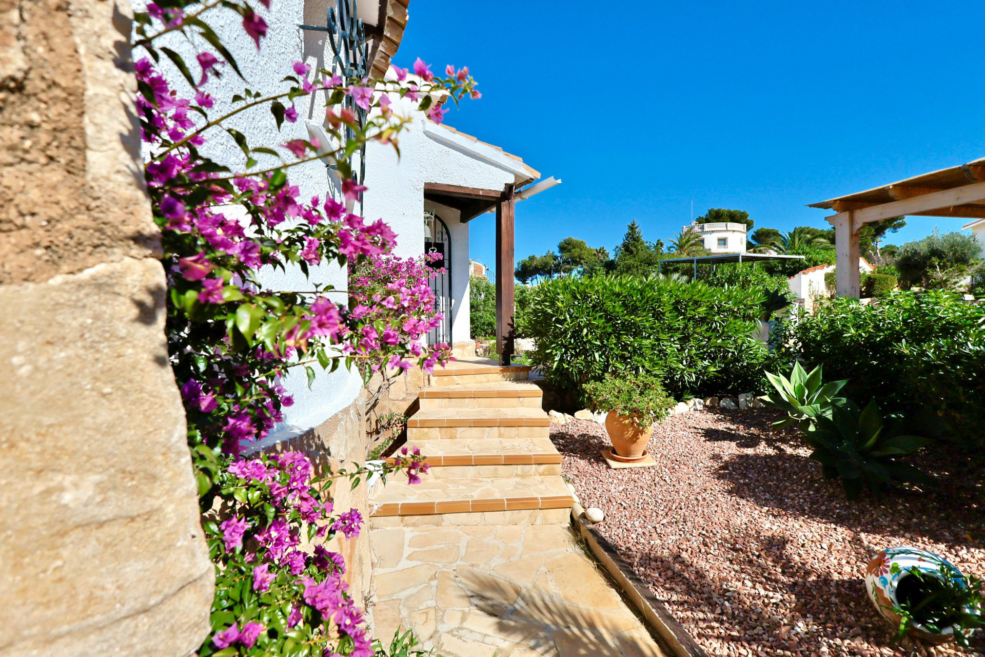 Villeneingang mit fuchsiafarbenen Bougainvillea und Kiesgarten.