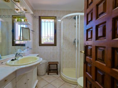 Badezimmerdetail mit gelbem Waschbecken, Eckdusche und geschnitzter Holztür.