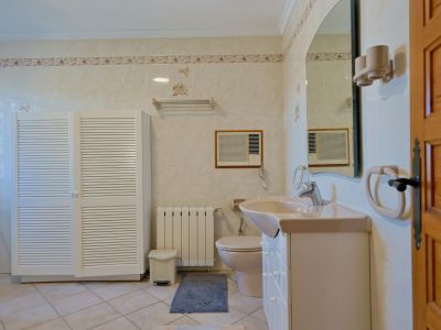 Gefliestes Badezimmer mit weißem Lamellenschrank und beigem Waschtisch.