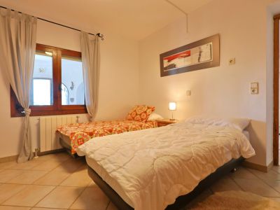 Helles Schlafzimmer mit Einzelbetten, Holzfensterrahmen und Fliesenboden.