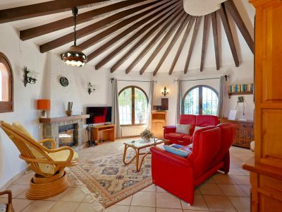 Rundes Wohnzimmer mit sichtbaren Holzbalken und Steinkamin.