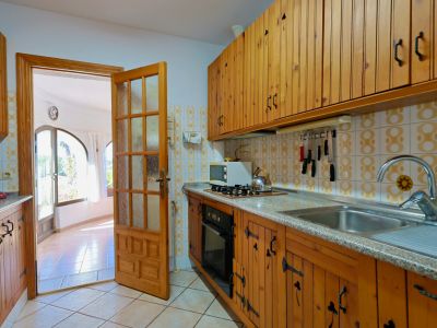 Rustikale Küche mit Holzschränken und Zugang zu einem hellen Wohnzimmer mit großen Fenstern.