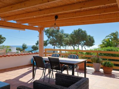 Überdachte Terrasse mit Meerblick und Essmöbeln.