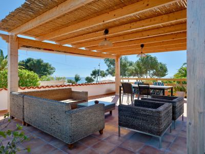 Überdachte Terrasse mit Rattanmöbeln und Meerblick.