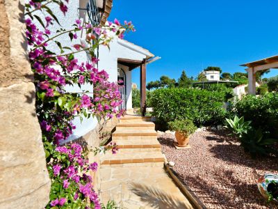 Villeneingang mit fuchsiafarbenen Bougainvillea und Kiesgarten.