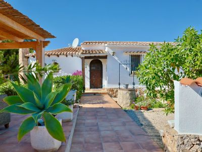 Villeneingang mit gefliestem Weg, mediterranem Grün und Steinbrunnen.