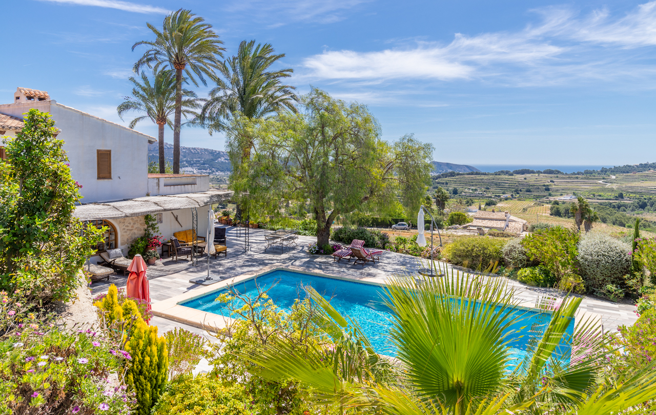 Außenpoolbereich mit Steinterrasse und mediterraner Bepflanzung, mit weitem Panoramablick über die Weinberge bis hin zur Küste von Moraira.