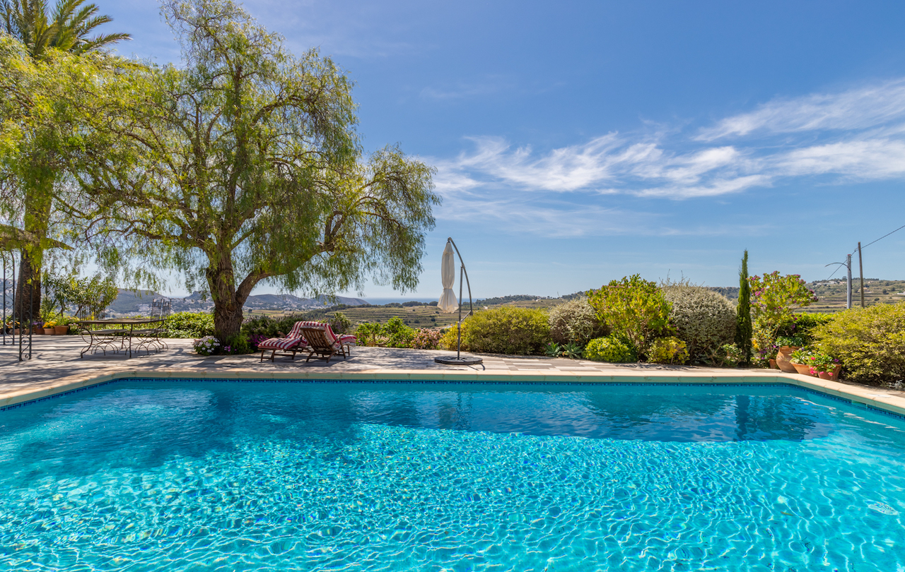 Großzügige Poolterrasse mit rutschfestem Belag, schattigem Ruhebereich unter Bäumen und Panoramablick über Weinberge bis hin zum Meer.