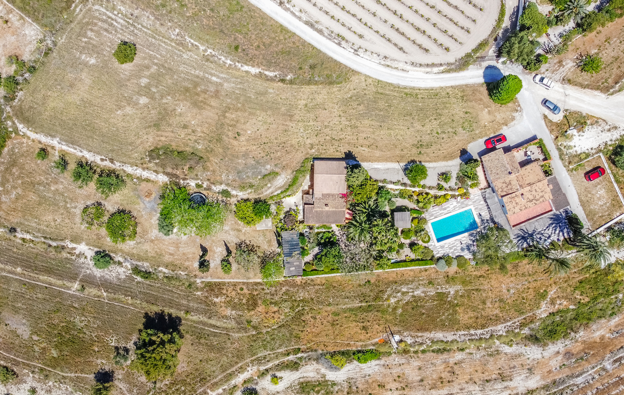 Luftbild des Anwesens, das die Anordnung der beiden Gebäude, den Pool mit Terrasse und die in die ländliche Landschaft integrierten Gärten zeigt.