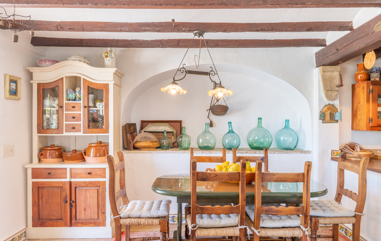 Rustikaler valencianischer Essbereich mit sichtbaren Holzbalken, traditionellem Geschirrschrank und einer dekorativen Nische mit Glasballons hinter der Sitzgruppe.