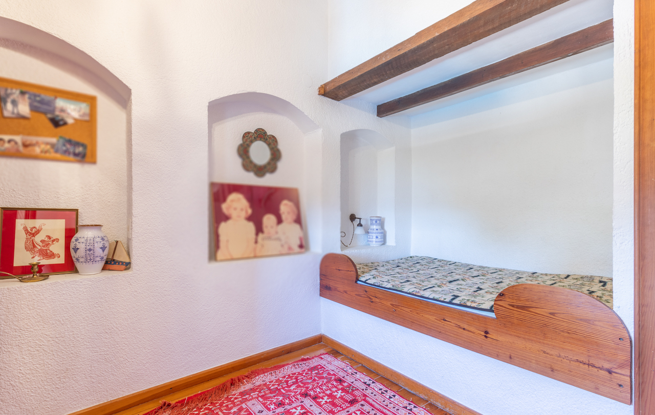 Rustikales Schlafzimmer mit eingebautem Holzbett, Sichtbalken und dekorativen Wandnischen in traditionell weiß verputzten Wänden.