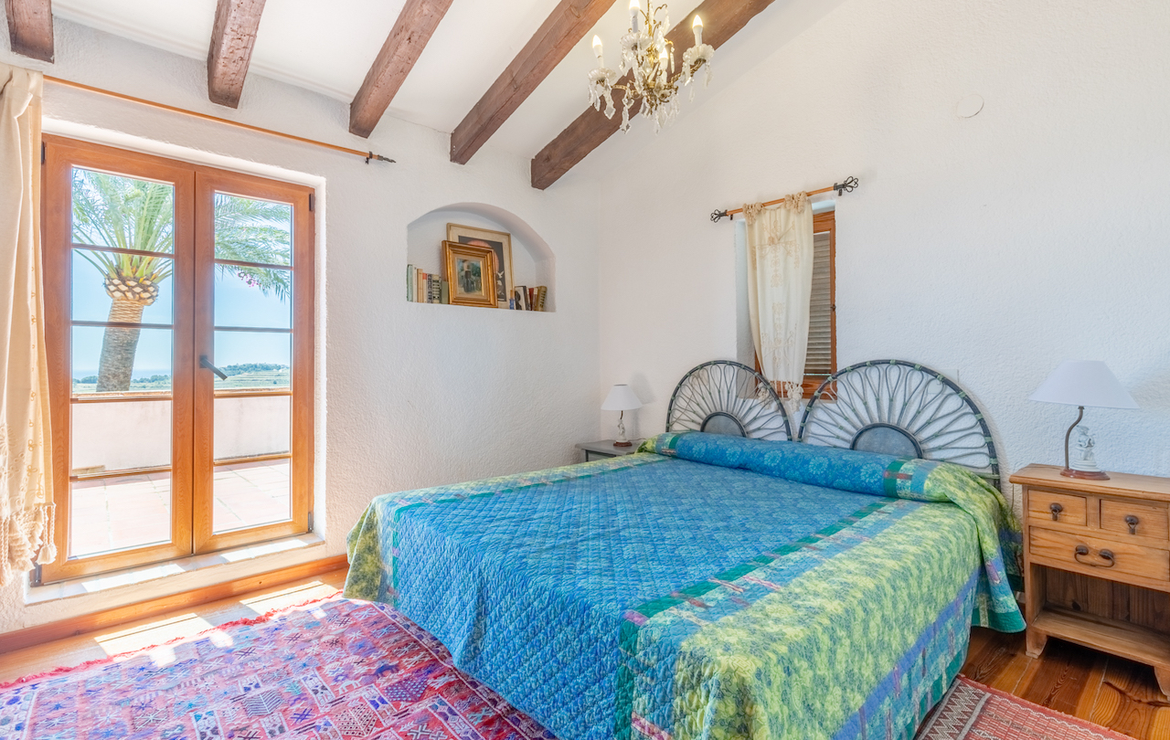Rustikales Schlafzimmer mit Sichtbalkendecke, Wandnische und direktem Zugang zur Terrasse mit Palmenblick. Ausgestattet mit Holzboden und schmiedeeisernem Kopfteil.