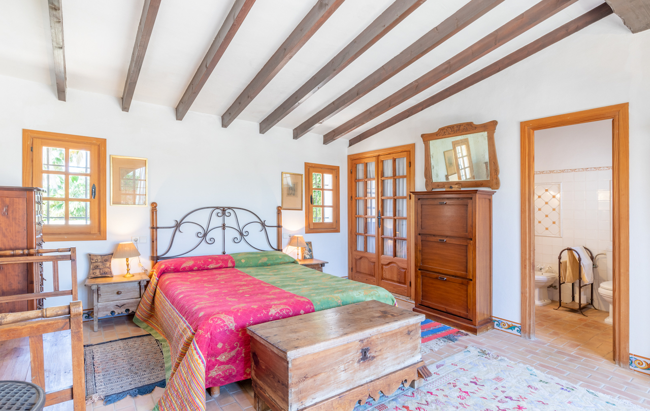 Rustikales Schlafzimmer mit sichtbaren Holzbalken, Terrakottaboden und traditionellen Möbeln. Das Zimmer bietet direkten Zugang zu einem integrierten Badezimmer.