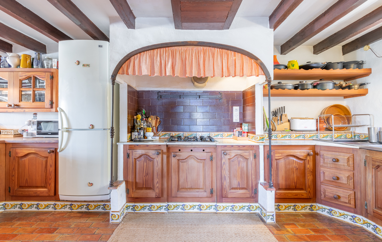 Traditionelle valencianische Küche mit sichtbaren Holzbalkendecken, Terrakottaböden und einem Kochbereich unter einem dekorativen Bogen mit kunstvollen Fliesen.