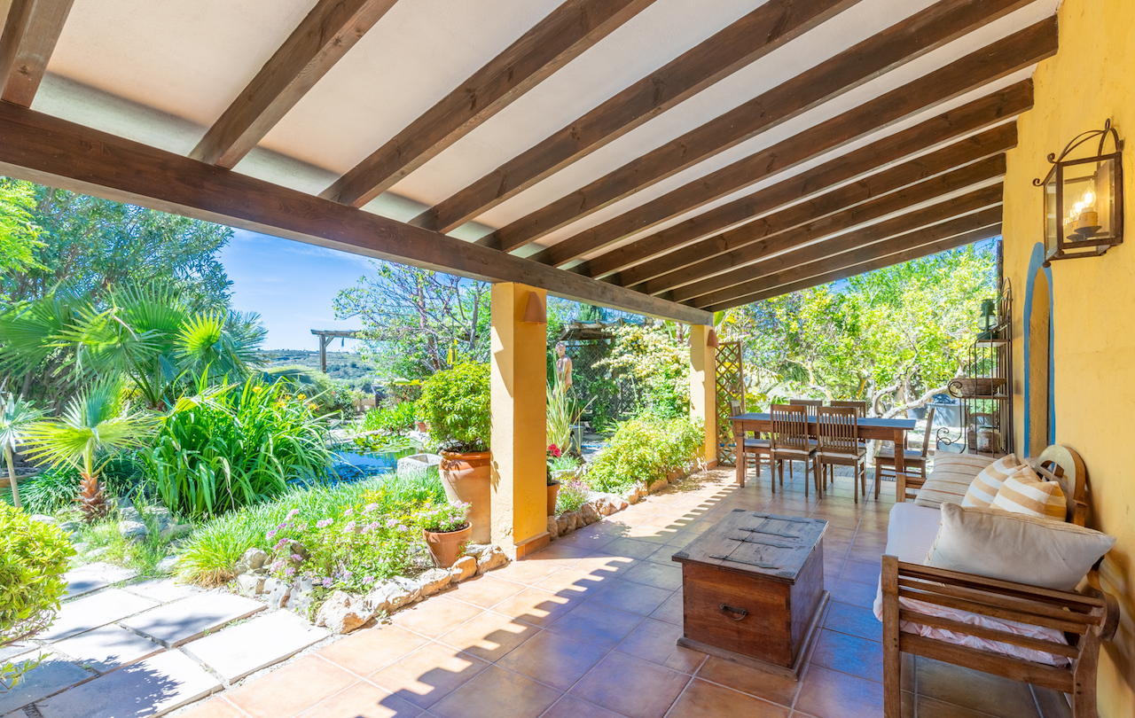 Überdachte Terrasse mit Holzbalkendecke, Terrakottaboden und Sitzbereich mit Blick auf den mediterranen Garten und einen Koiteich.
