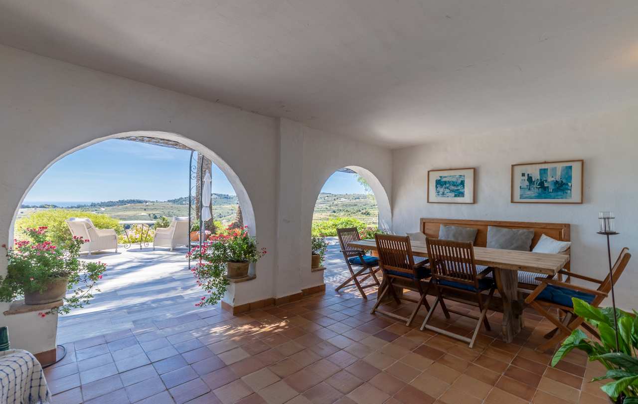 Überdachte Terrasse mit traditionellen Rundbögen, Terrakottaboden und rustikalem Essbereich. Sie bietet einen weiten Blick auf die Weinberge und das Mittelmeer.