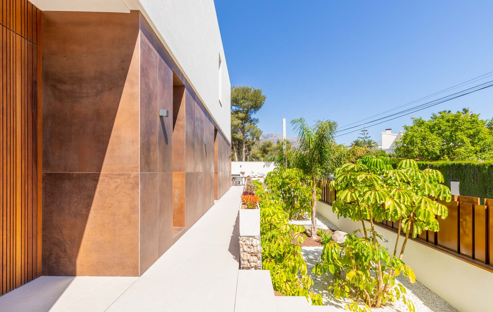 Außenansicht der Villa mit mediterranem Garten und erdfarbener Wandverkleidung.