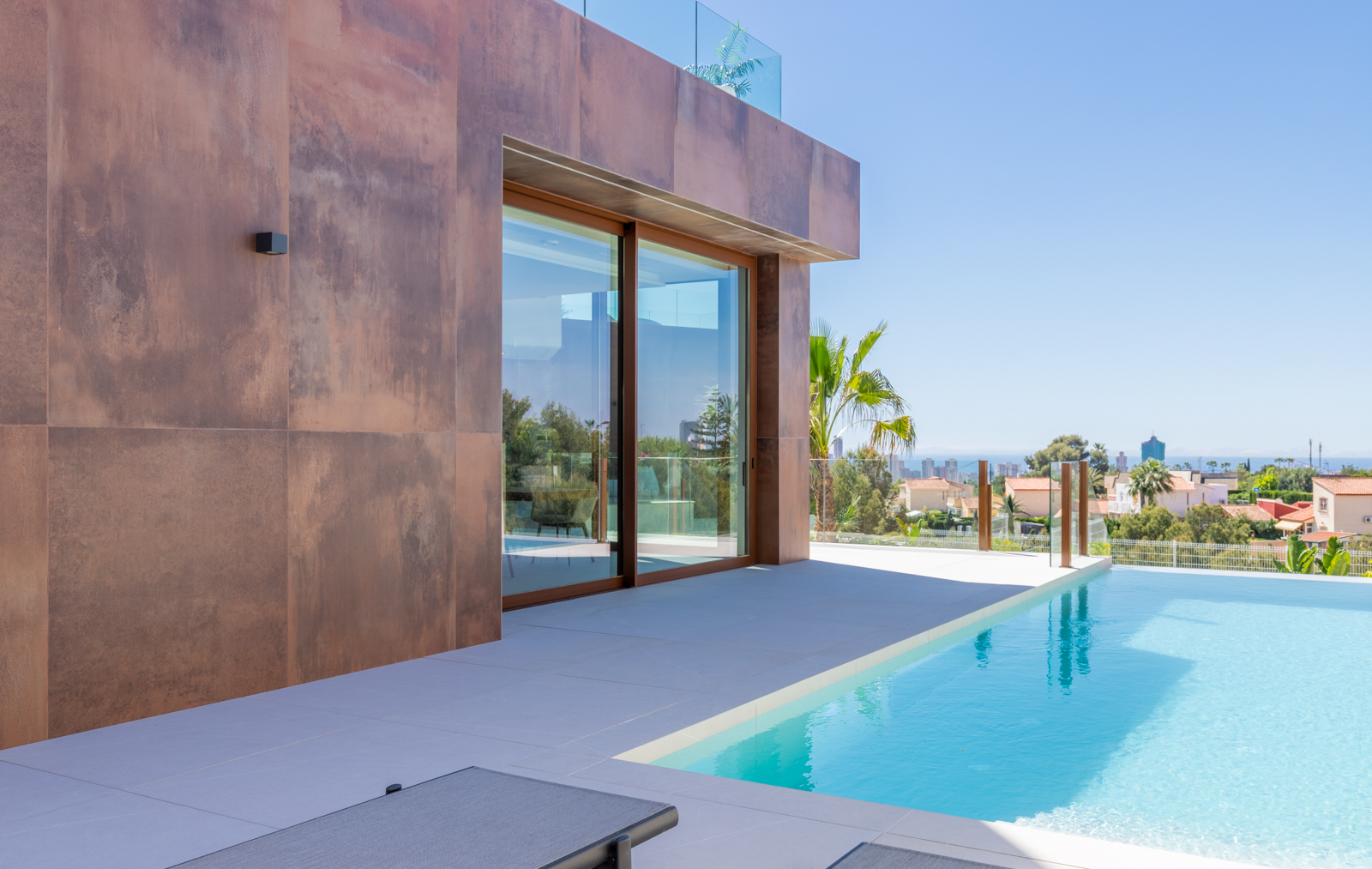 Blick auf den Infinity-Pool mit Fassade aus rostfarbenen Paneelen und Panoramablick auf die Stadt.