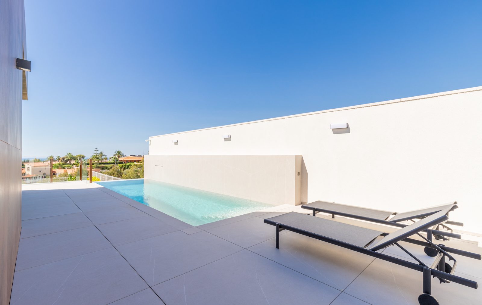 Detail des Infinity-Pools mit Aussicht und Liegestühlen auf grauen Fliesen.